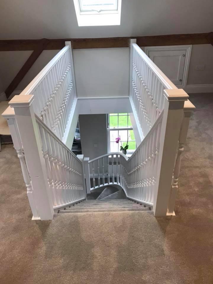 Two‑flight white balustrade staircase with a central turn and grey carpet