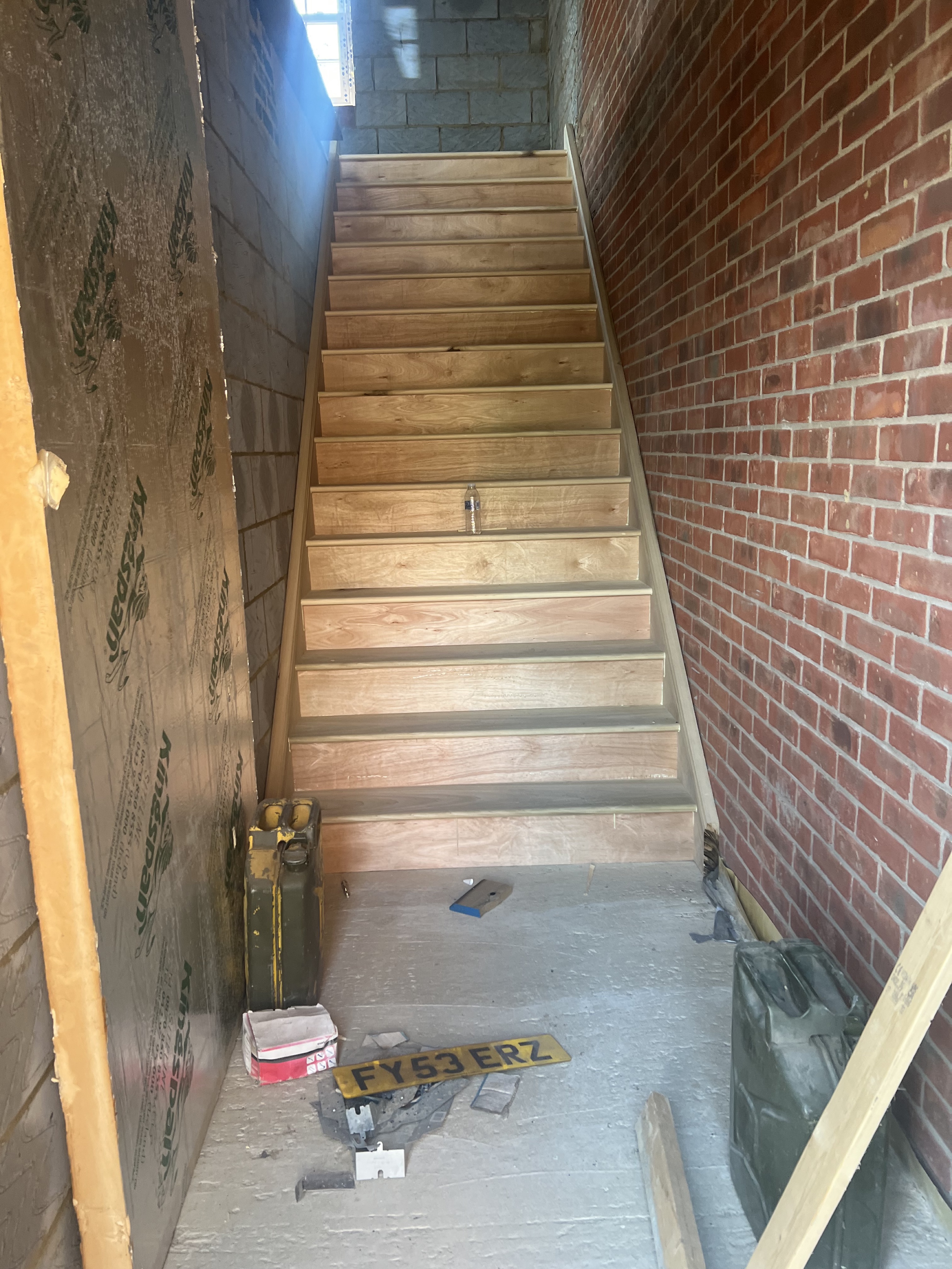 Straight oak staircase under construction within a brick‑lined site